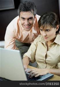 Portrait of a mature man smiling with a mid adult woman using a laptop beside him