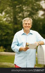 Portrait of a mature man standing beside a mailbox and holding mails