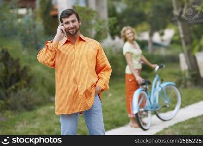 Portrait of a mature man talking on a mobile phone with a mature woman standing behind him with a bicycle
