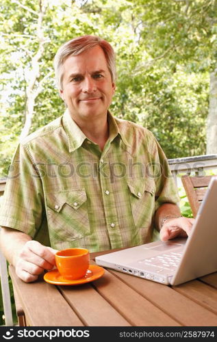 Portrait of a mature man using a laptop and holding a cup