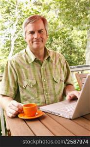 Portrait of a mature man using a laptop and holding a cup