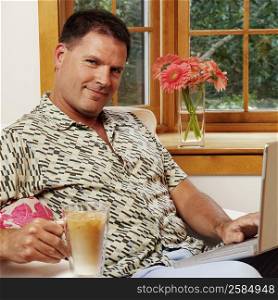 Portrait of a mature man using a laptop and holding a mug of coffee