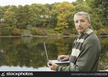 Portrait of a mature man using a laptop at the lakeside