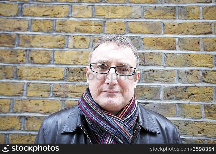 Portrait of a mature man wearing glasses with scarf against wall