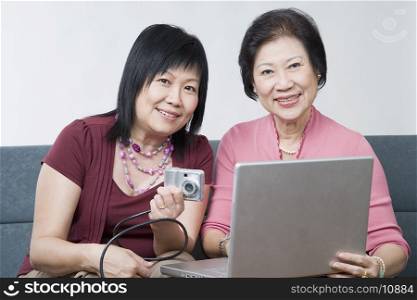 Portrait of a mature woman and a senior woman sitting with a digital camera connected to a laptop
