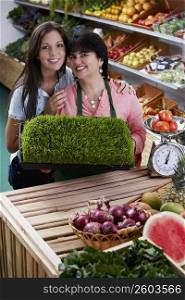 Portrait of a mature woman and her daughter standing with a tray of wheatgrass in a grocery store and smiling