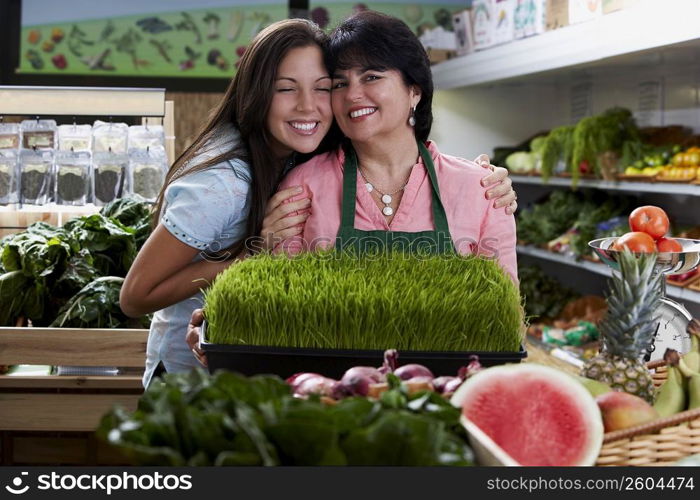 Portrait of a mature woman and her daughter standing with a tray of wheatgrass in a grocery store and smiling