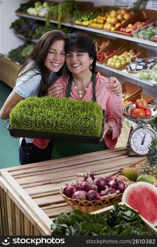 Portrait of a mature woman and her daughter standing with a tray of wheatgrass in a grocery store and smiling