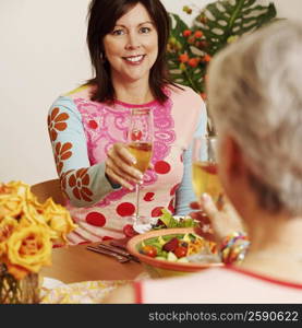 Portrait of a mature woman and her friend toasting with a champagne flute at a dining table