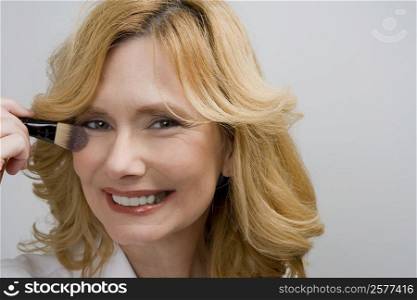 Portrait of a mature woman applying blush on her cheek and smiling