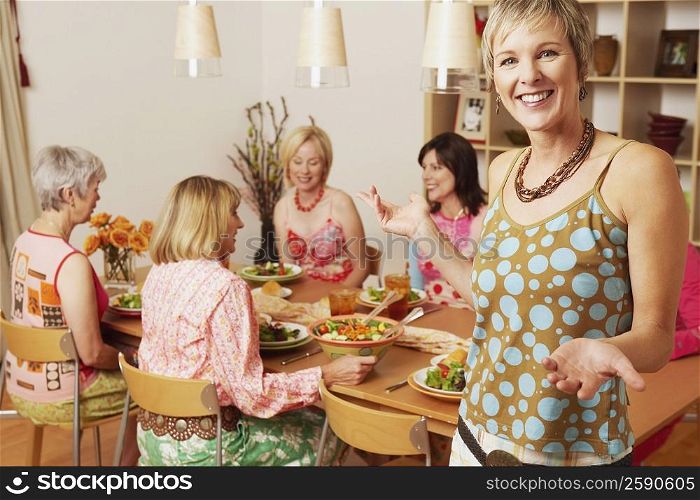 Portrait of a mature woman gesturing and her friends sitting at the dining table in the background