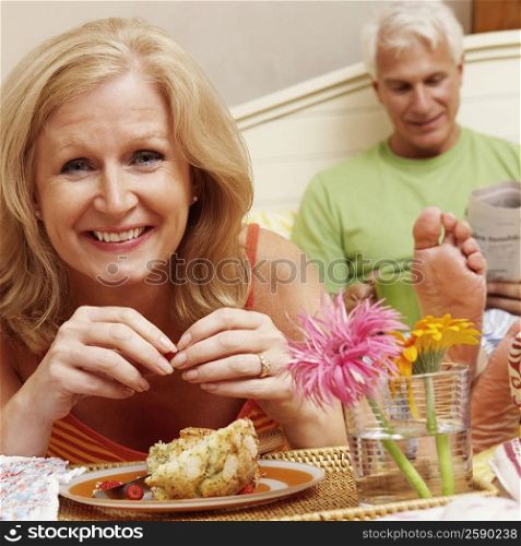 Portrait of a mature woman having breakfast in bed with a mature man sitting behind her