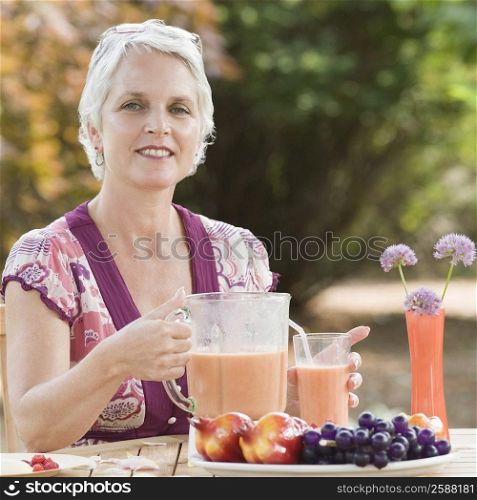 Portrait of a mature woman holding a blender filled with juice