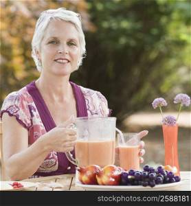 Portrait of a mature woman holding a blender filled with juice