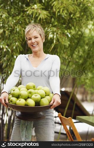 Portrait of a mature woman holding a bowl of granny smith apples