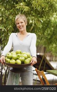 Portrait of a mature woman holding a bowl of granny smith apples