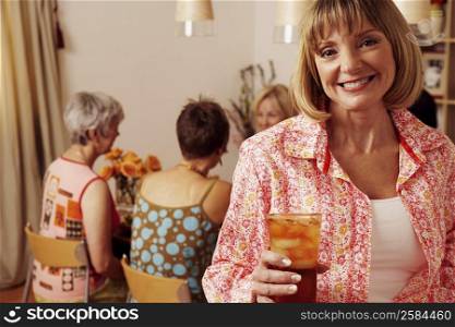 Portrait of a mature woman holding a cocktail and her friends sitting behind her