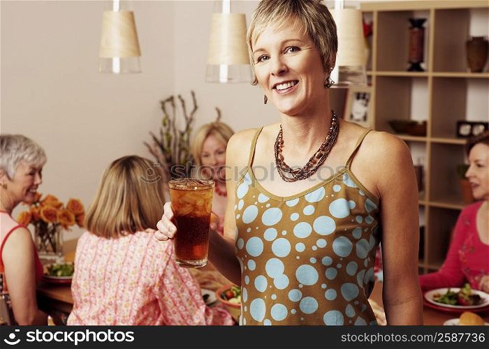 Portrait of a mature woman holding a glass of cocktail and her friends sitting at a dining table in the background