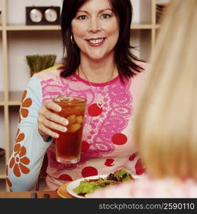 Portrait of a mature woman holding a glass of cocktail with her friend and smiling
