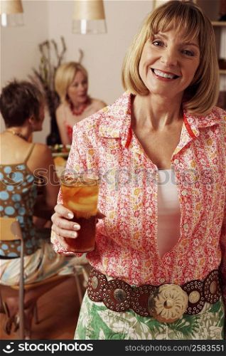 Portrait of a mature woman holding a glass with her friends sitting behind her