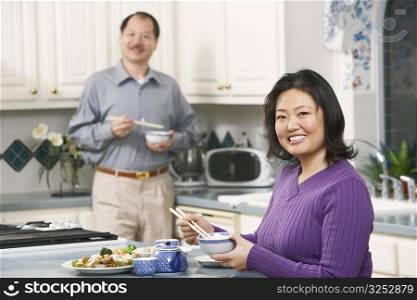 Portrait of a mature woman holding a pair of chopsticks with a senior man standing behind her