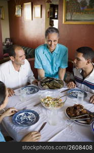 Portrait of a mature woman holding a plate of food with her family sitting at the dining table