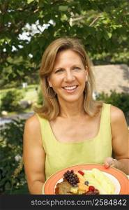 Portrait of a mature woman holding a plate of fruit salad and smiling