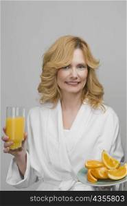 Portrait of a mature woman holding a plate of oranges and a glass of orange juice