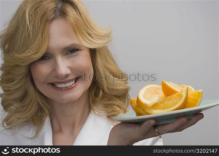 Portrait of a mature woman holding a plate of oranges and smiling
