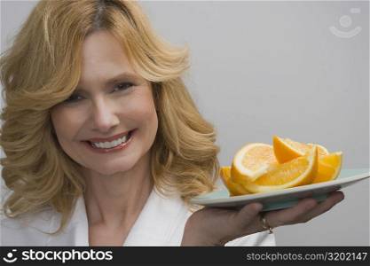 Portrait of a mature woman holding a plate of oranges and smiling