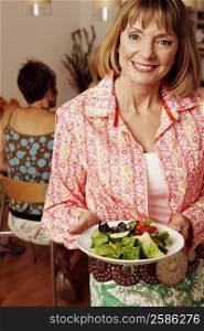 Portrait of a mature woman holding a plate of salad and her friend sitting behind her