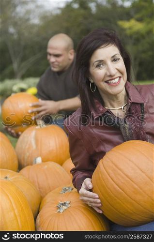 Portrait of a mature woman holding a pumpkin and smiling with a mid adult man standing in the background