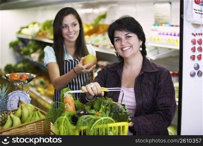 Portrait of a mature woman holding a shopping basket and a female sales clerk giving her a mango