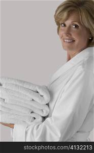 Portrait of a mature woman holding a stack of folded towels and smiling