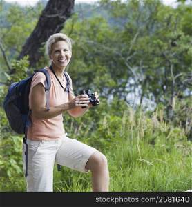 Portrait of a mature woman holding binoculars in a forest and smiling