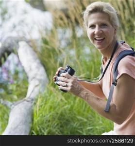 Portrait of a mature woman holding binoculars in a forest and smiling
