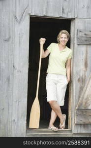 Portrait of a mature woman leaning against a door and holding an oar