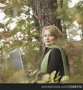Portrait of a mature woman leaning against a tree and using a laptop