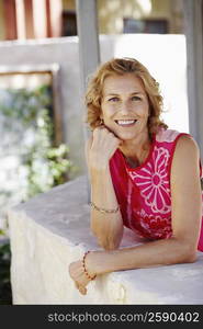 Portrait of a mature woman leaning against a wall with her hand on her chin and smiling