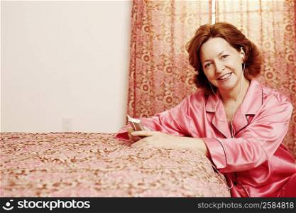 Portrait of a mature woman leaning against the bed and listening to an MP3 player