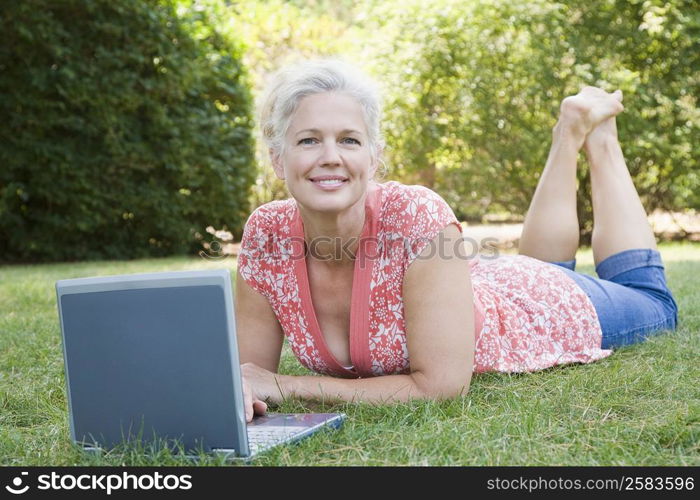 Portrait of a mature woman lying in a park and using a laptop