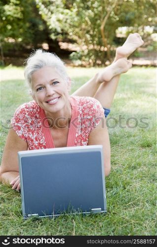Portrait of a mature woman lying in a park and using a laptop