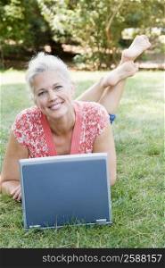 Portrait of a mature woman lying in a park and using a laptop