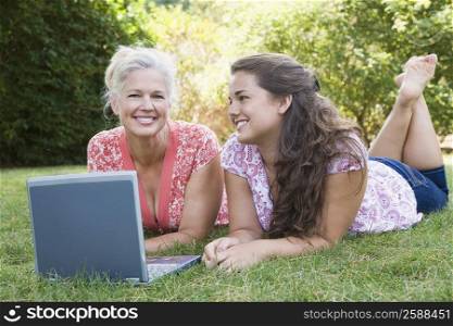 Portrait of a mature woman lying in a park with her daughter and using a laptop