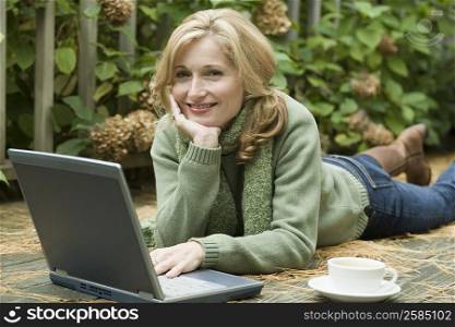 Portrait of a mature woman lying in front of a laptop and smiling