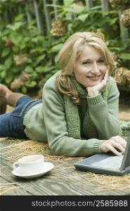 Portrait of a mature woman lying in front of a laptop and smiling