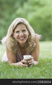 Portrait of a mature woman lying on grass and holding a coffee cup