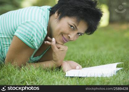 Portrait of a mature woman lying on grass with a book and smiling