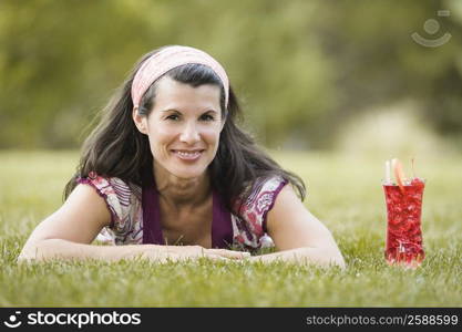 Portrait of a mature woman lying on grass with a glass of juice beside her