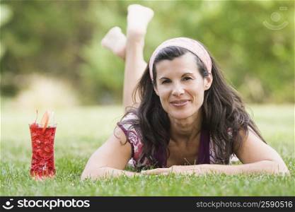 Portrait of a mature woman lying on grass with a glass of juice beside her